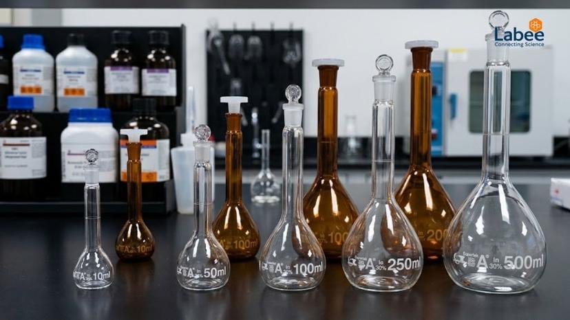 Bộ sưu tập bình định mức thủy tinh trong suốt và thủy tinh nâu Supertek đặt trên bàn Lab